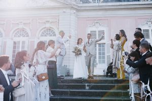 Wedding ceremony guests gather on steps of an elegant white building with pink accents.