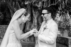 Black and white photo captures exchange of rings during outdoor wedding ceremony.