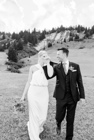 A romantic wedding photo captured in black and white against a mountainous landscape with evergreen trees.