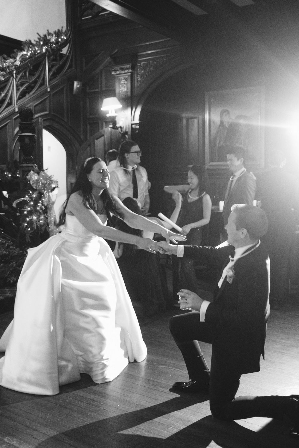 A bride in a white ballgown holds hands with a dancing partner during a festive wedding reception.