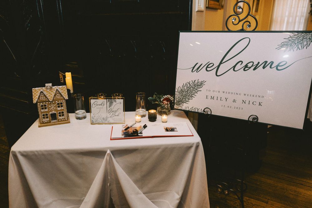 Wedding welcome table with decorative signage and small house display on white tablecloth.