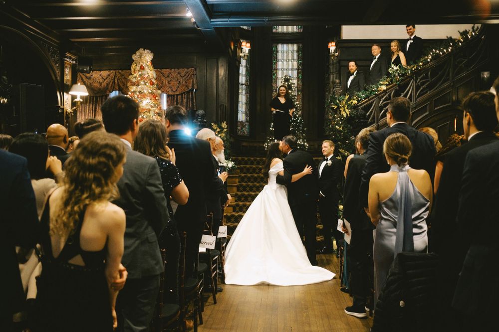 Wedding guests mingle and dance in an ornate dark wood venue with warm lighting.