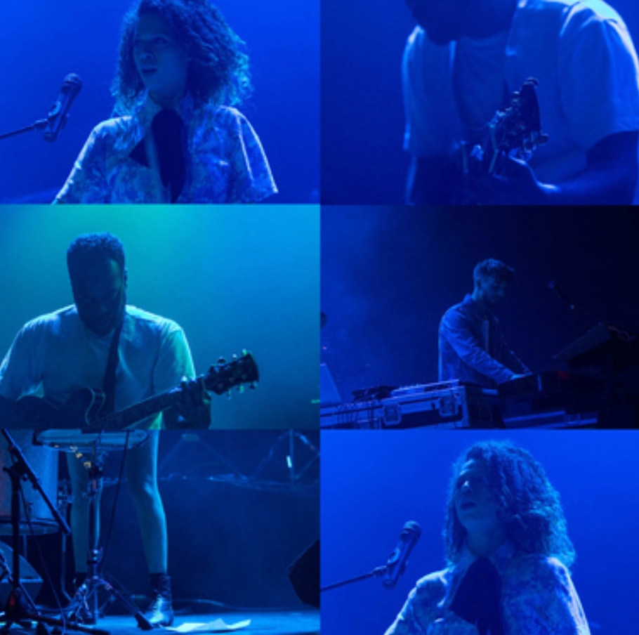 Musicians perform on stage under dramatic blue lighting during a live concert performance.