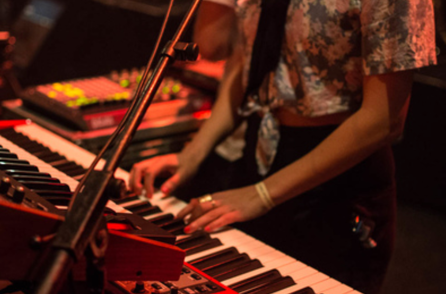 Close-up shot of hands playing a keyboard with a microphone stand visible in dim red lighting.