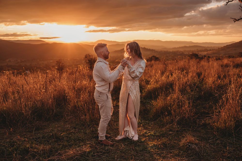 Couple embracing in field during golden sunset with mountains in background.