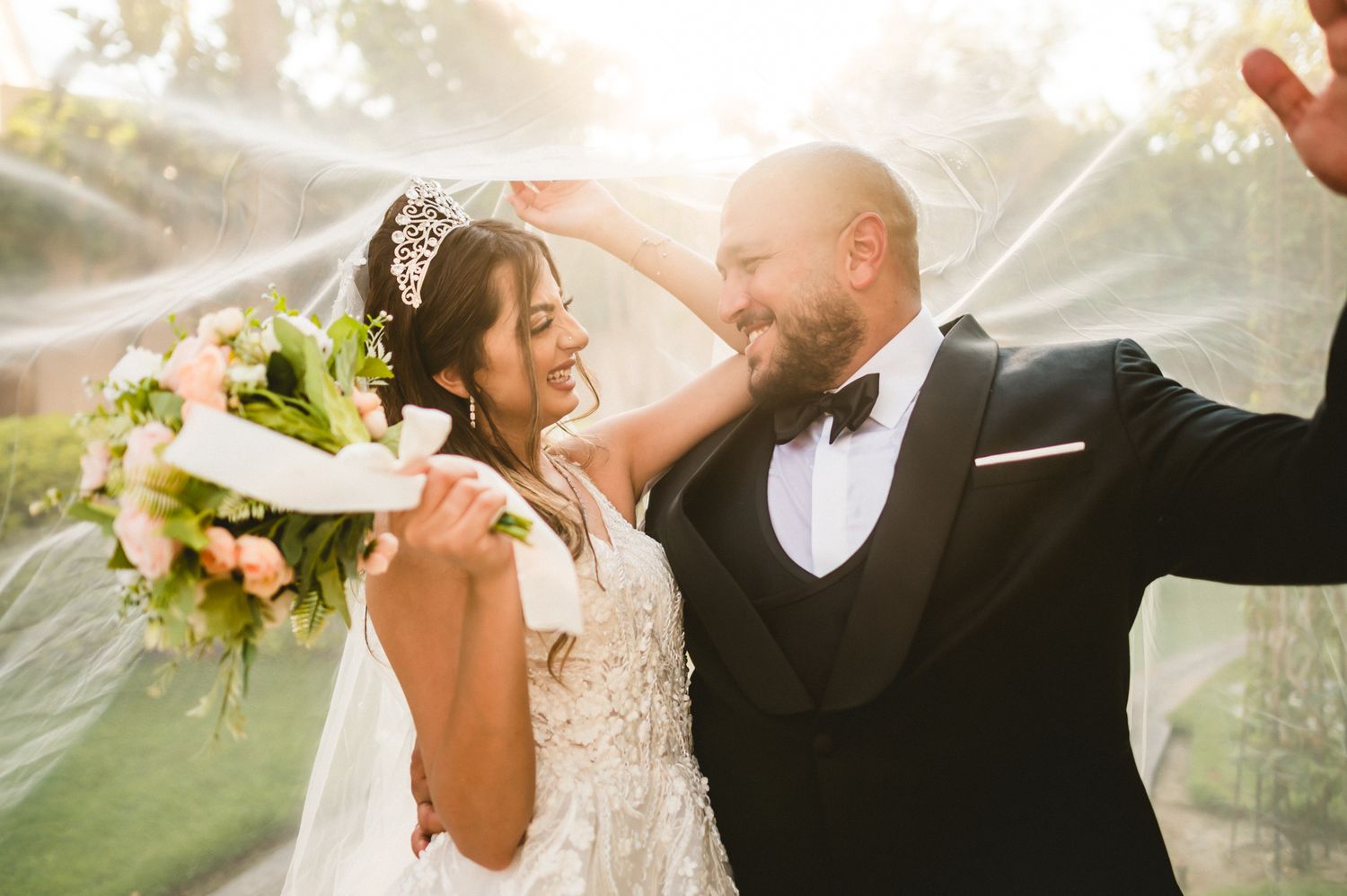 A joyful wedding couple shares a candid moment outdoors in golden sunlight.