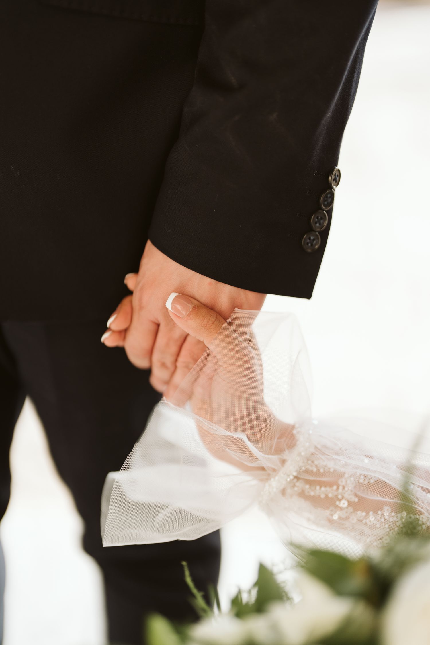 Close-up photo of newlyweds holding hands with lace veil detail and formal attire.