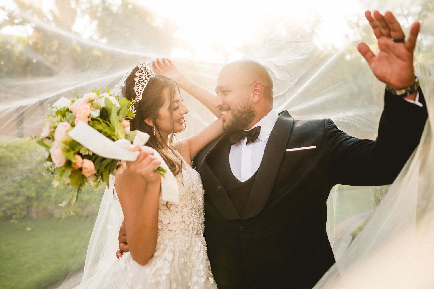 A celebratory moment between newlyweds with flowing veil catching sunlight.