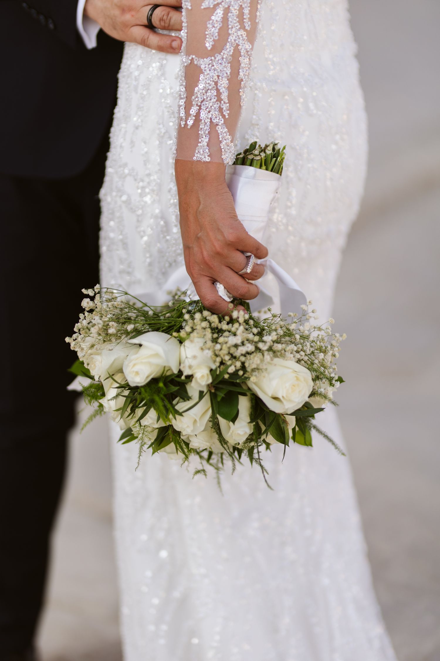 White roses and baby's breath bouquet held against a detailed lace wedding dress.