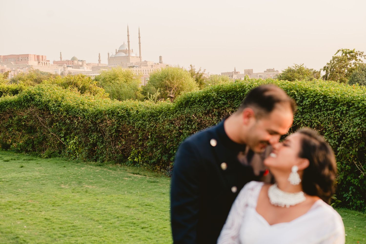 A romantic wedding portrait with historic architecture and gardens in the background.