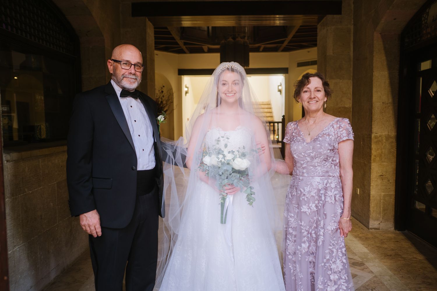 A formal wedding portrait taken in an elegant indoor venue with stone columns.