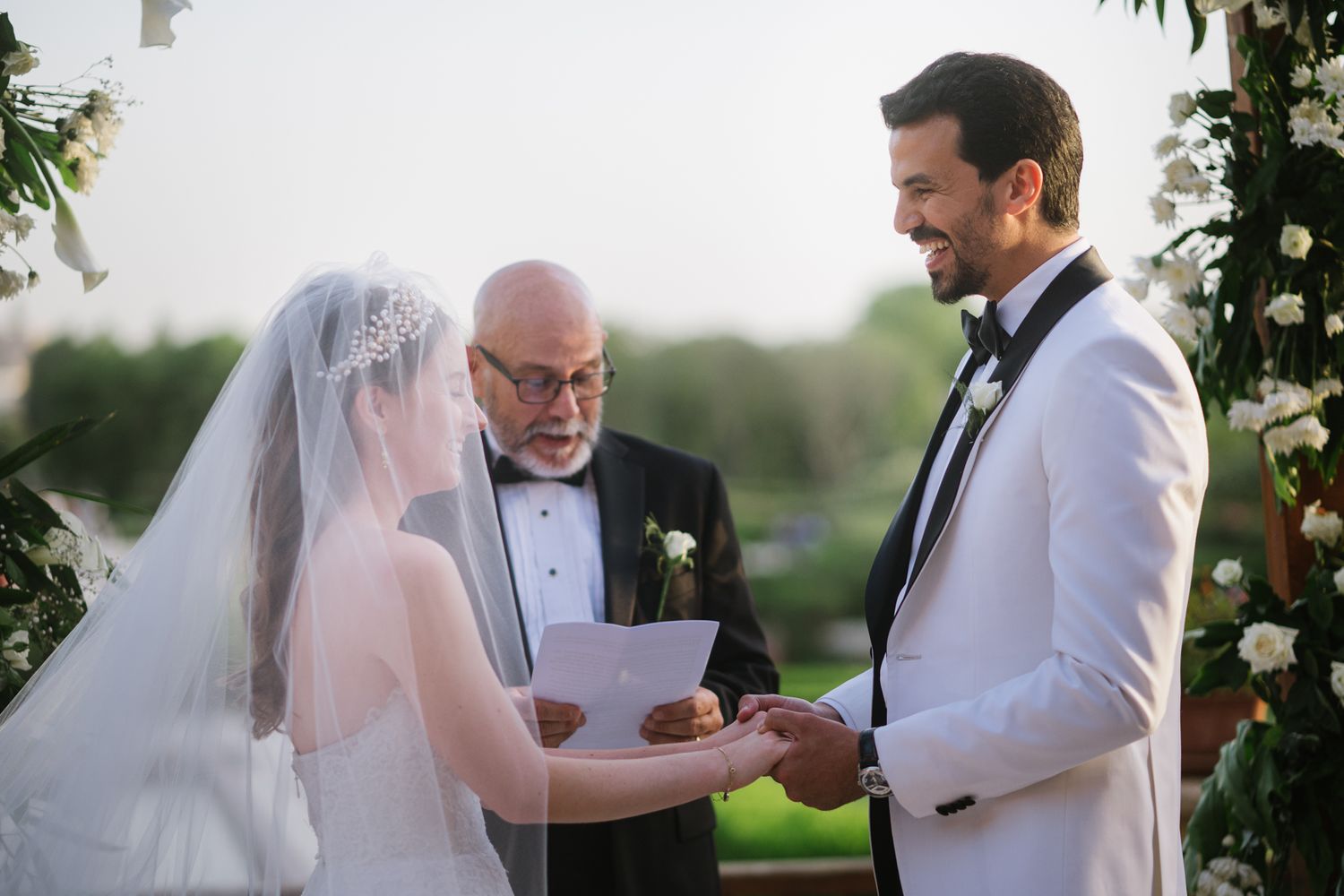 A wedding ceremony moment with couple exchanging vows under a floral archway at sunset.