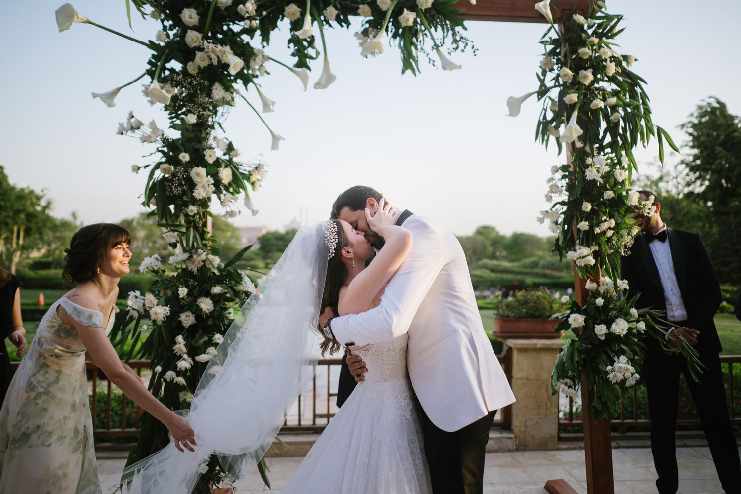 A wedding celebration under a floral arch decorated with white blooms and greenery.