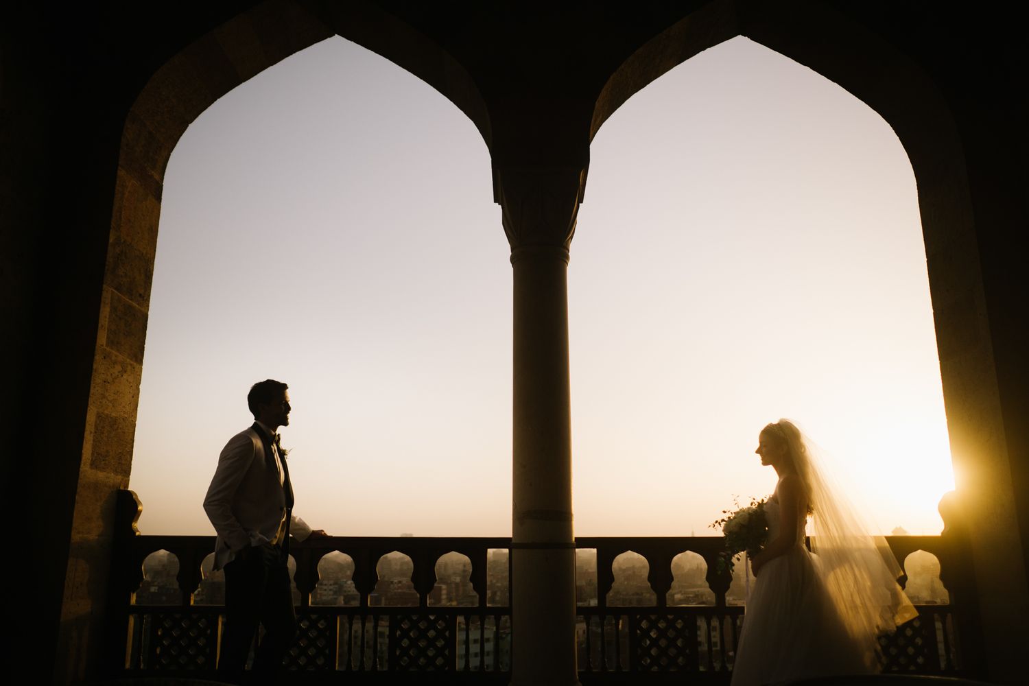 Two silhouettes share a moment at sunset through ornate Gothic arches.