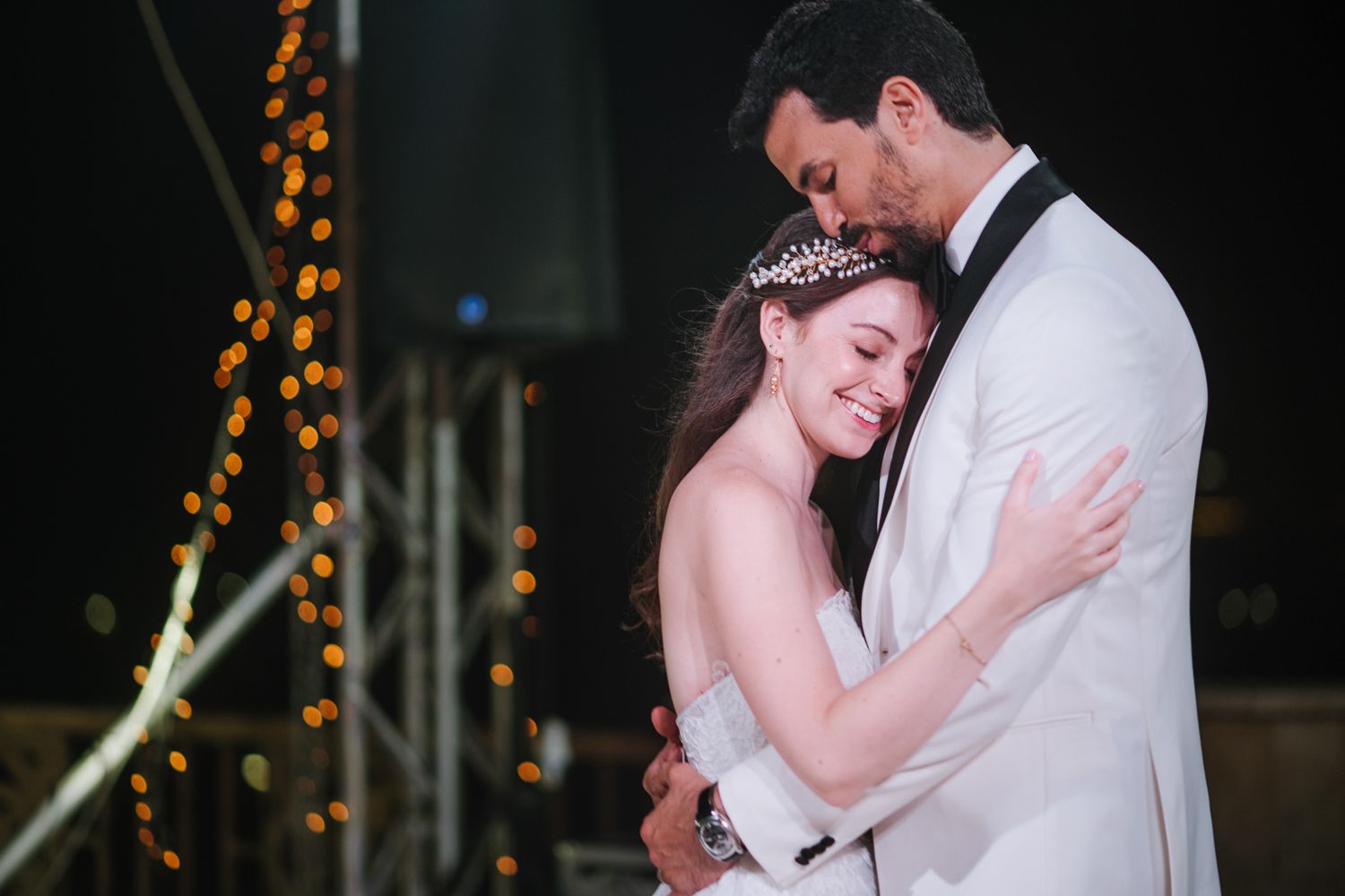Romantic moment during wedding reception with twinkling lights in background.