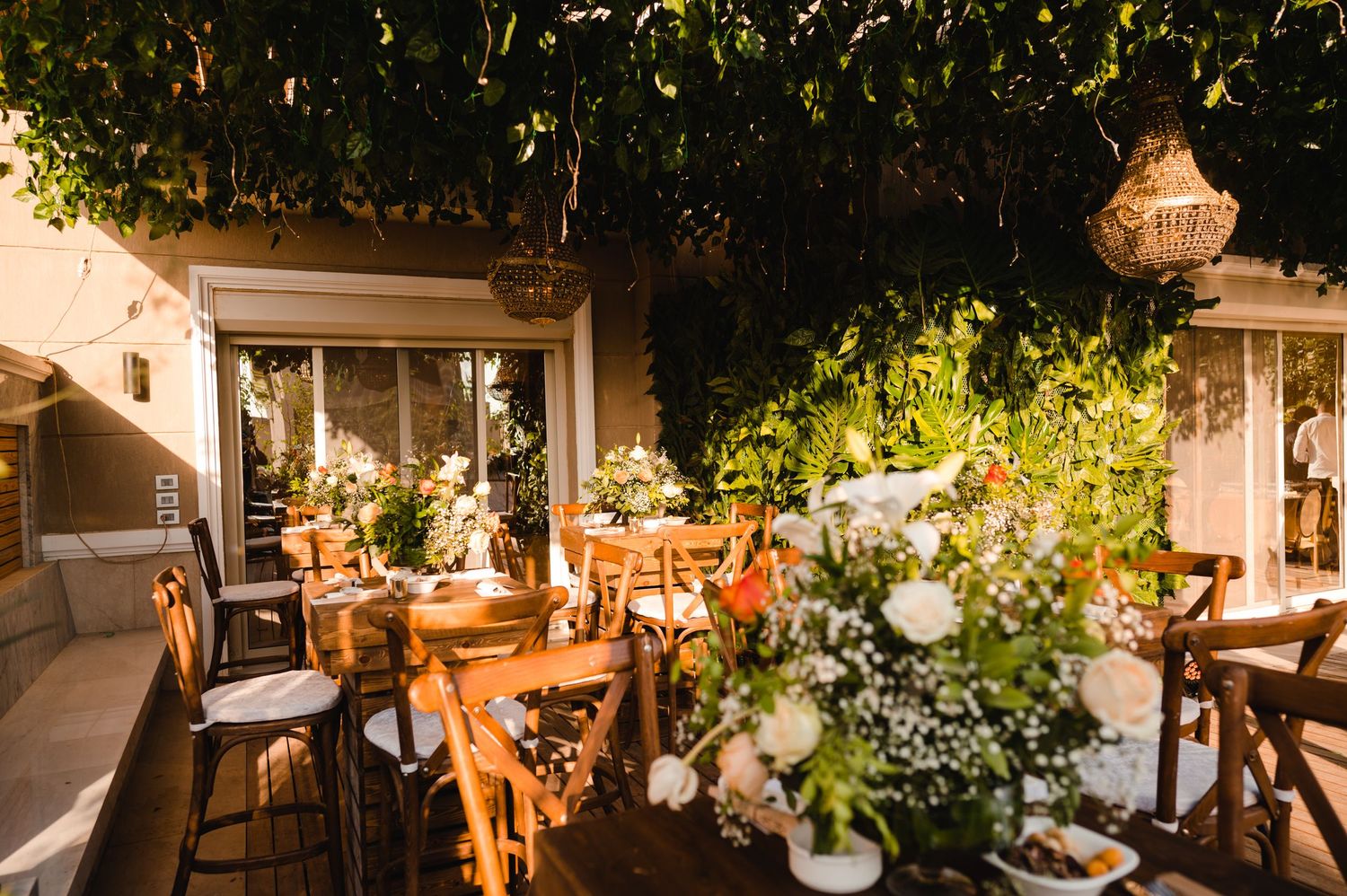 Rustic outdoor dining area with wooden chairs and floral arrangements under natural canopy.