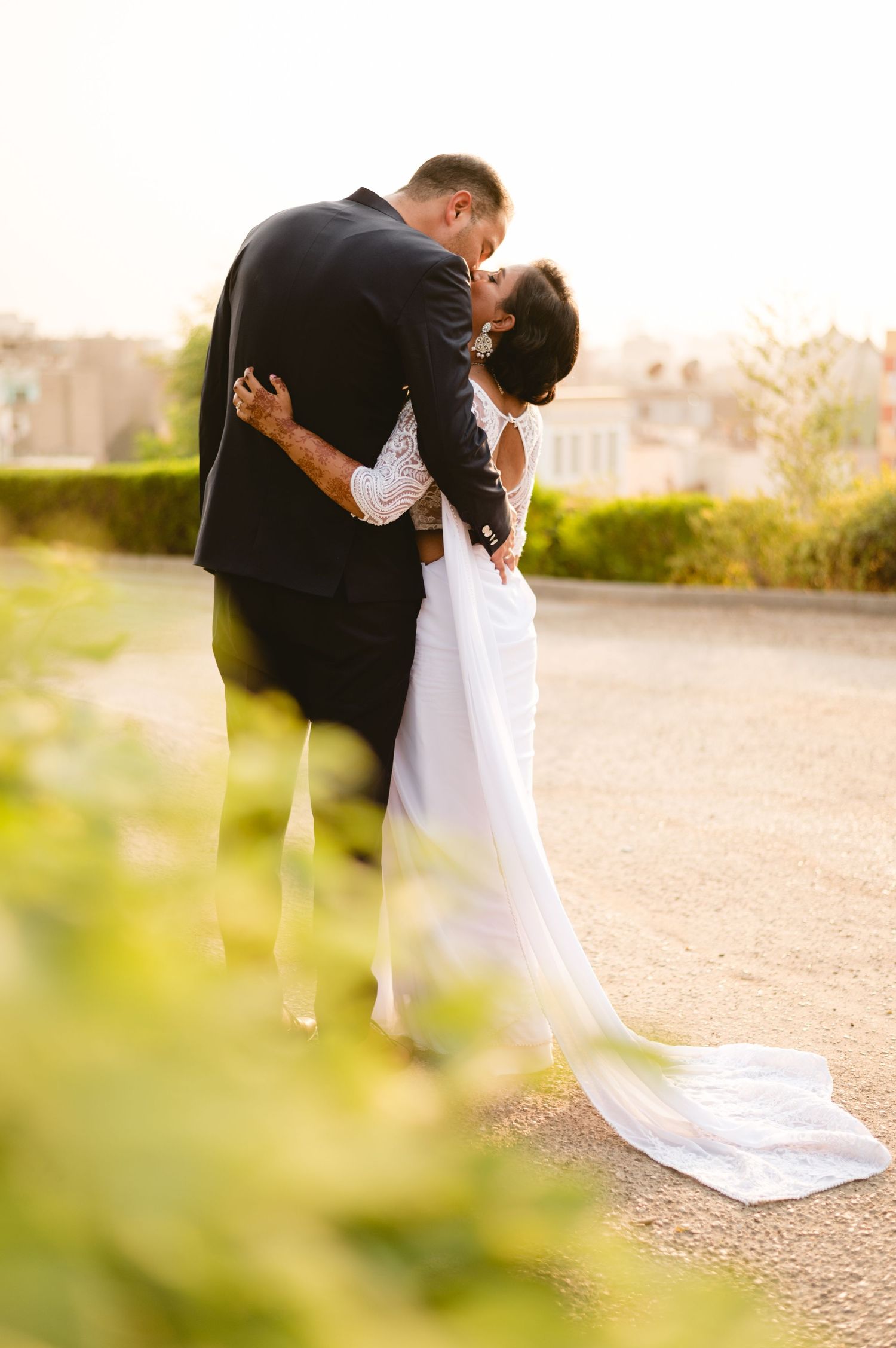 A romantic embrace captured through garden foliage with flowing white dress details.