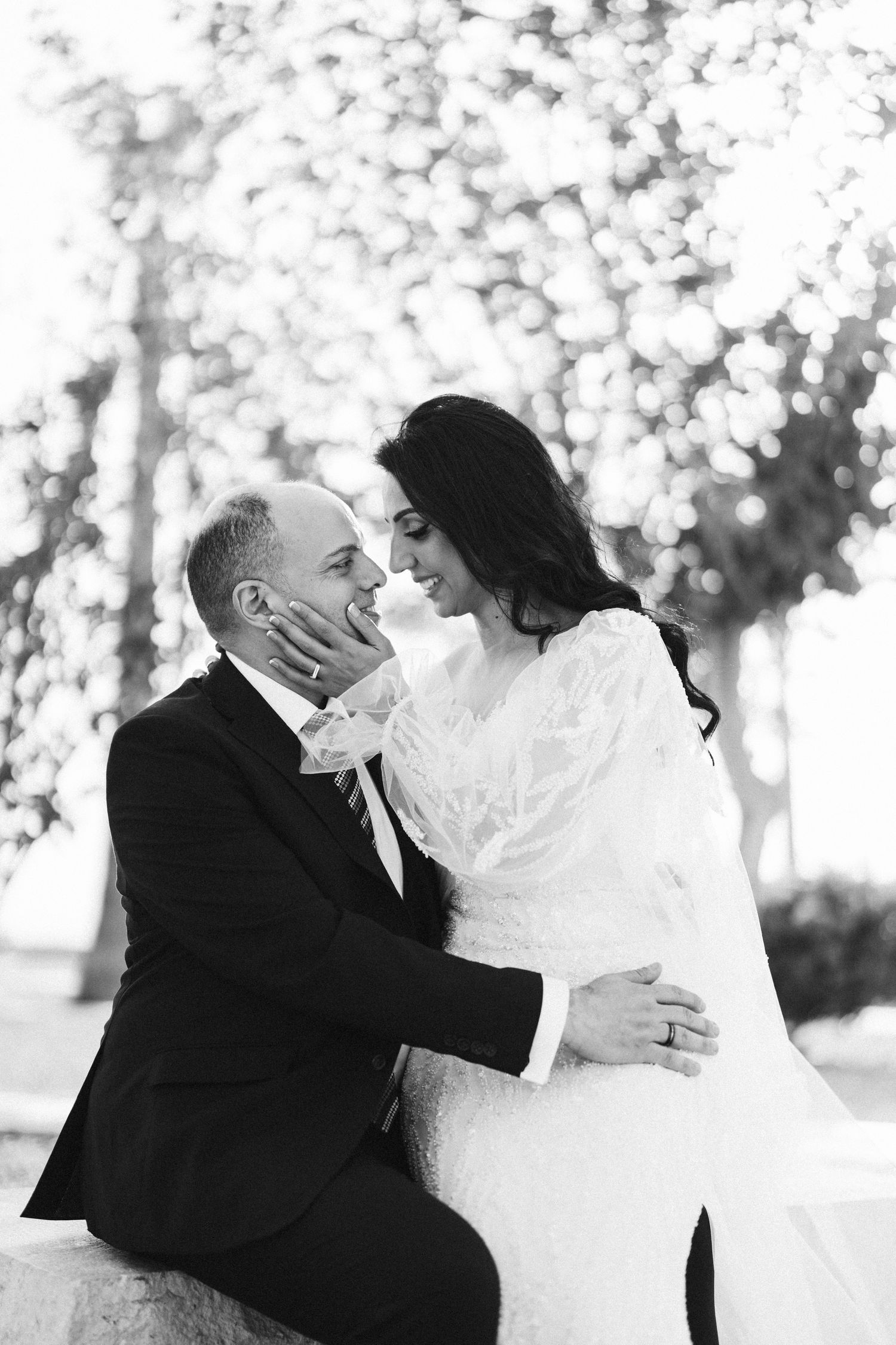 Black and white portrait of newlyweds sharing an intimate moment under bokeh lighting.