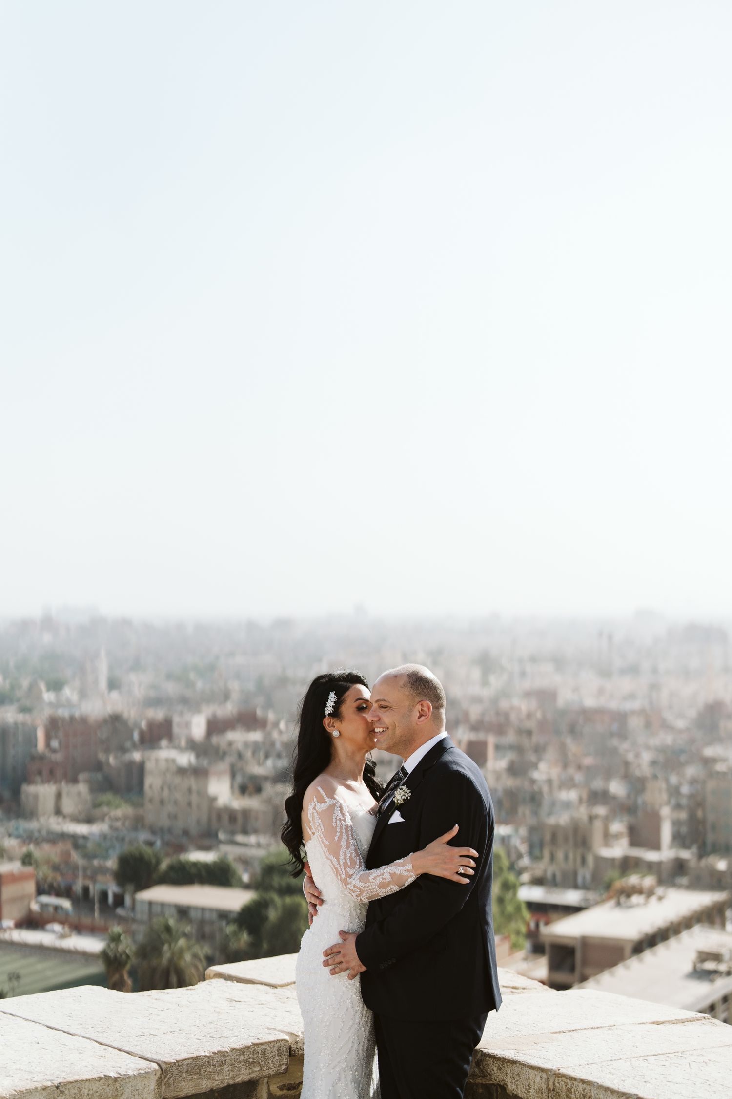 Wedding couple sharing an intimate moment on a rooftop with a cityscape in the background.
