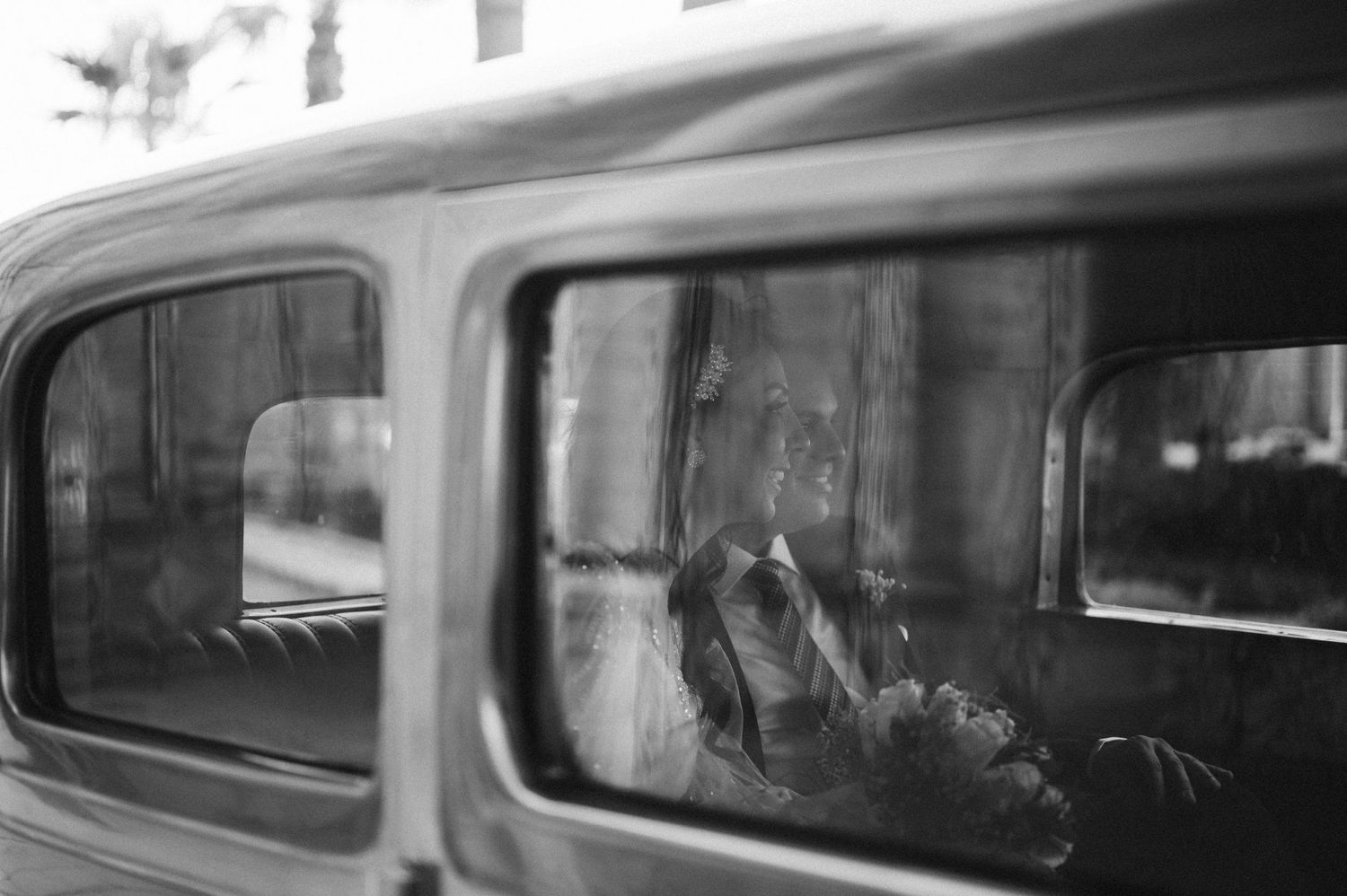 A black and white vintage-style photo through a car window capturing a wedding moment.