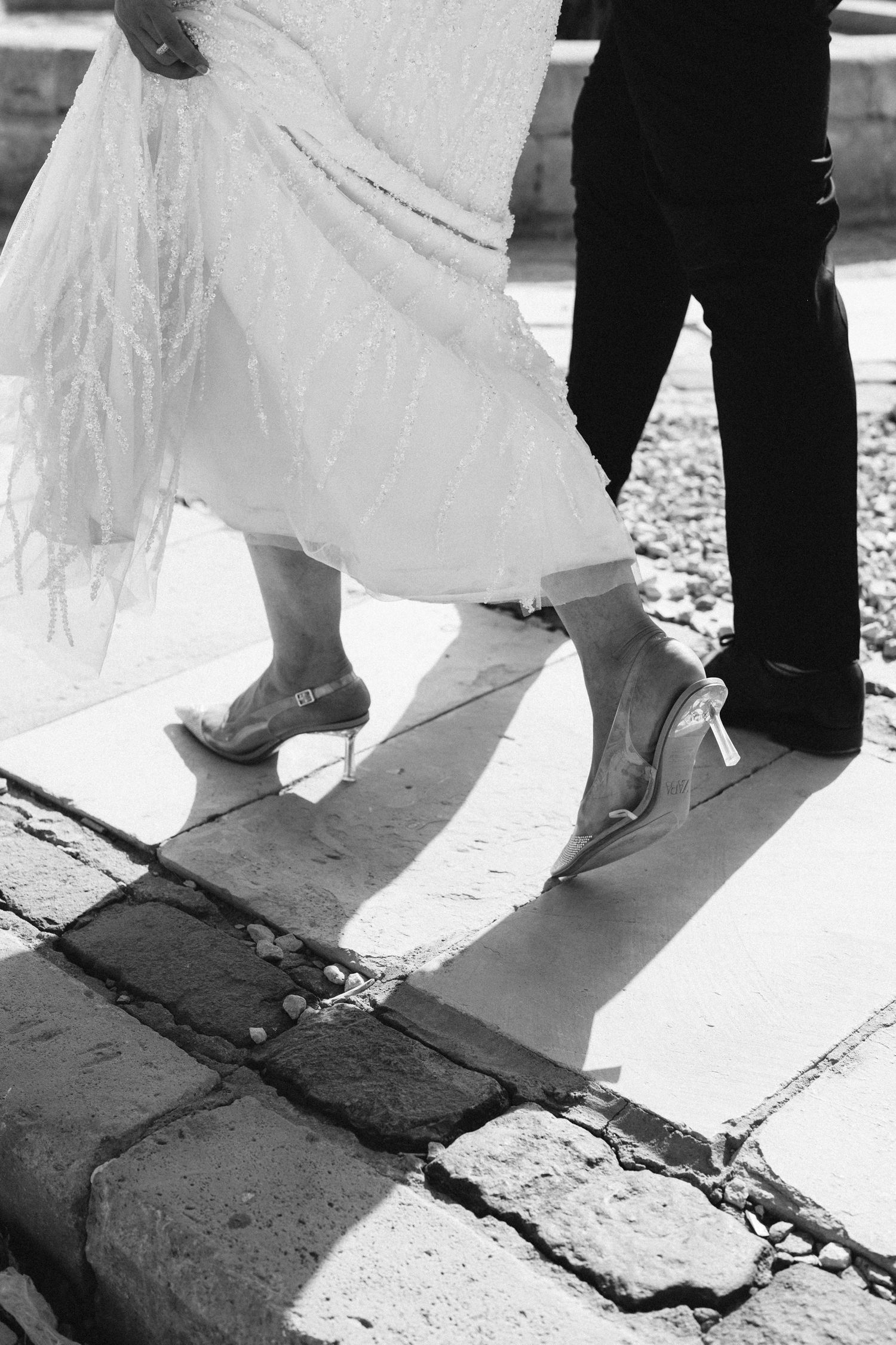 Black and white photo of bride and groom's feet dancing, with her white dress flowing in motion.