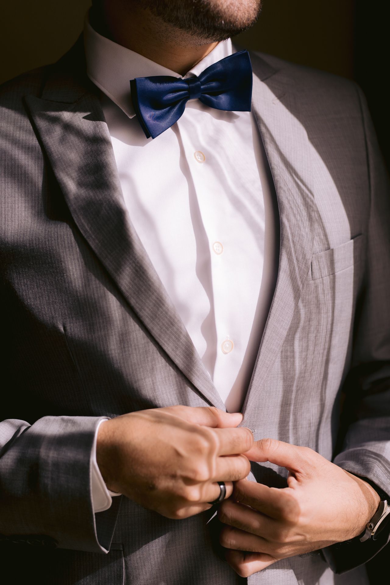 Close-up of groom's formal attire featuring gray suit and navy blue bow tie.