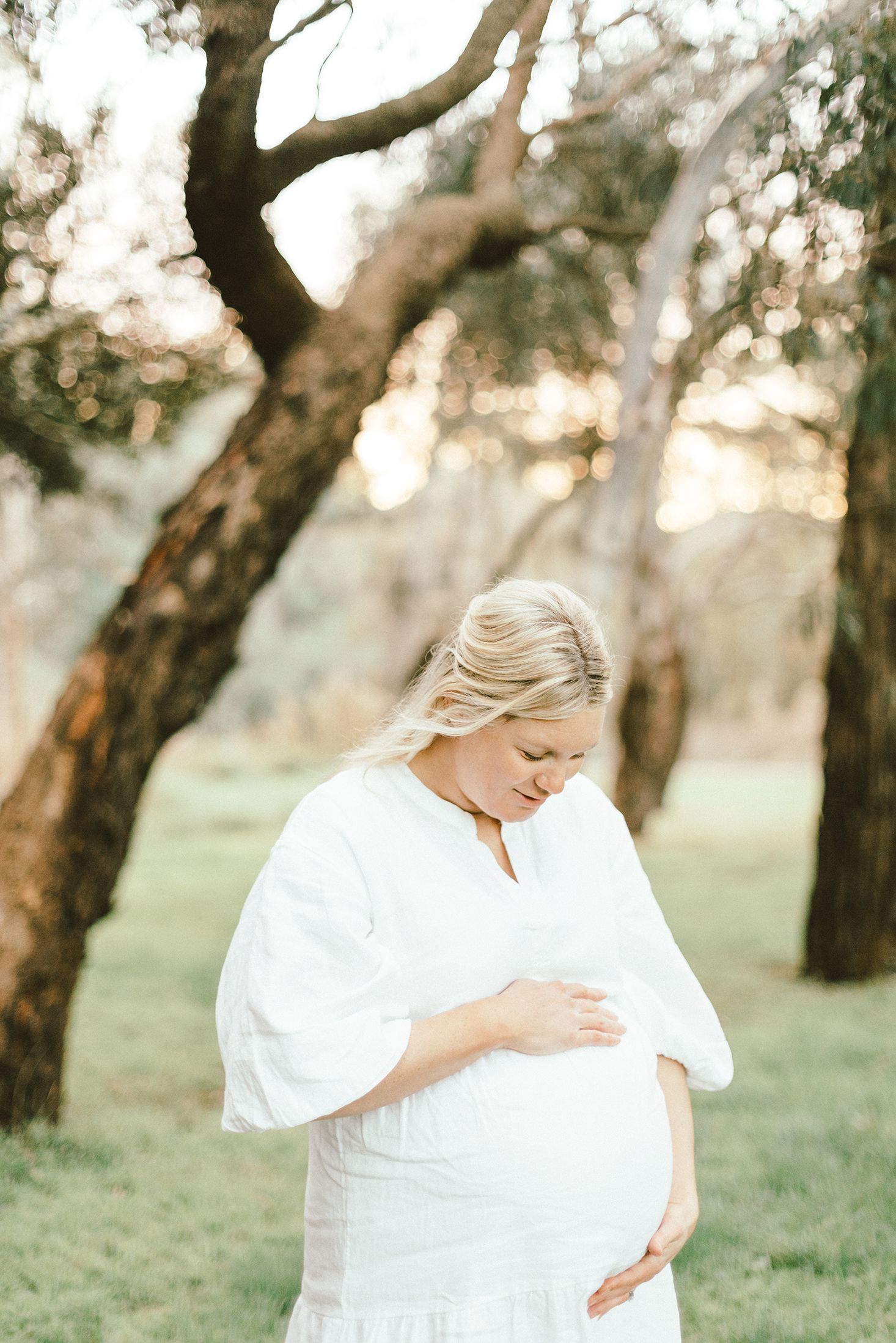 Peaceful maternity portraits in nature featuring woman in white dress cradling her growing belly.