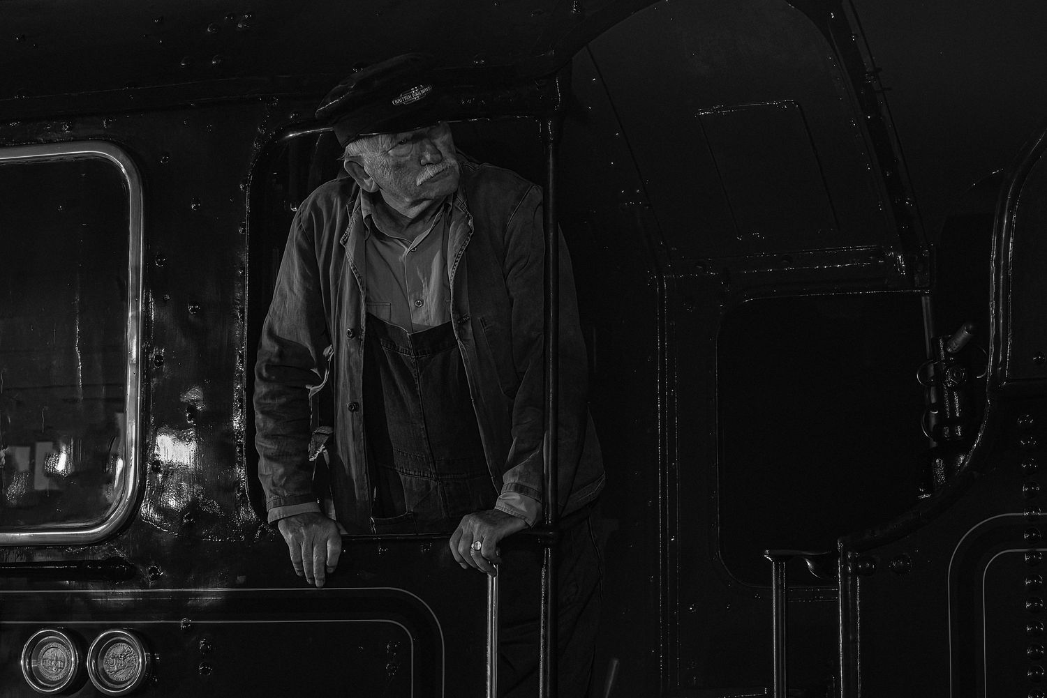 Vintage black and white photo of a train conductor in the cab of a steam locomotive.
