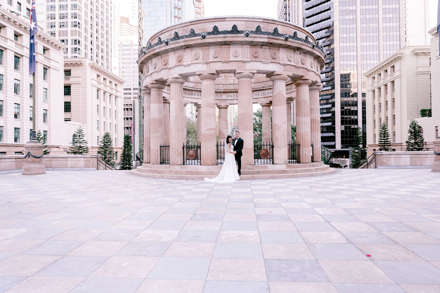 Elegant wedding photo at columned rotunda in urban setting with tall buildings.