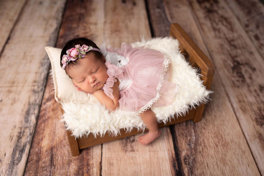 Sleeping newborn in pink tulle dress on fluffy white blanket during professional photography session.
