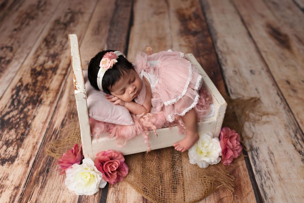 Sleeping infant in pink dress on wooden bed with floral decorations.