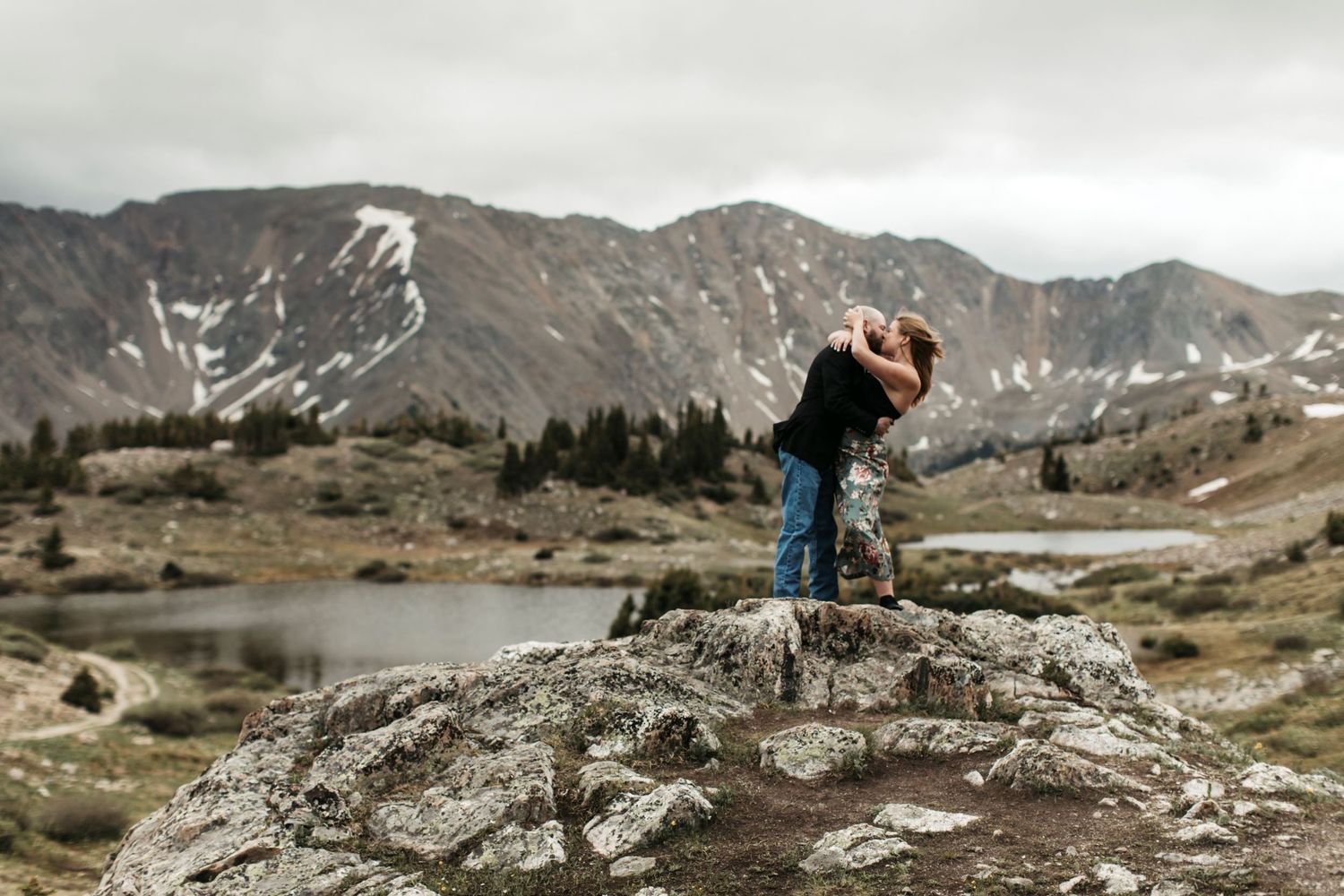 Couple kissing while standing on rocks in front of rocks and a snowy mountain