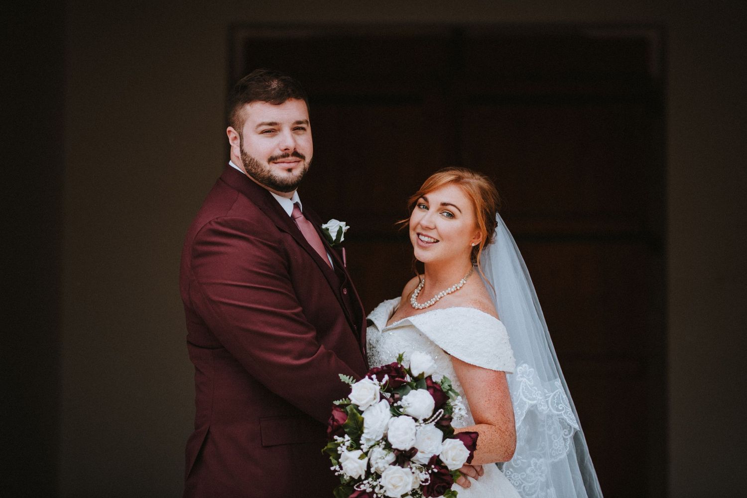 A formal wedding portrait featuring burgundy and white floral details.