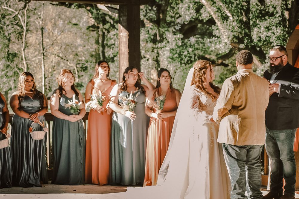 Wedding ceremony outdoors with bridesmaids wearing mixed color dresses standing in a line during the ceremony.