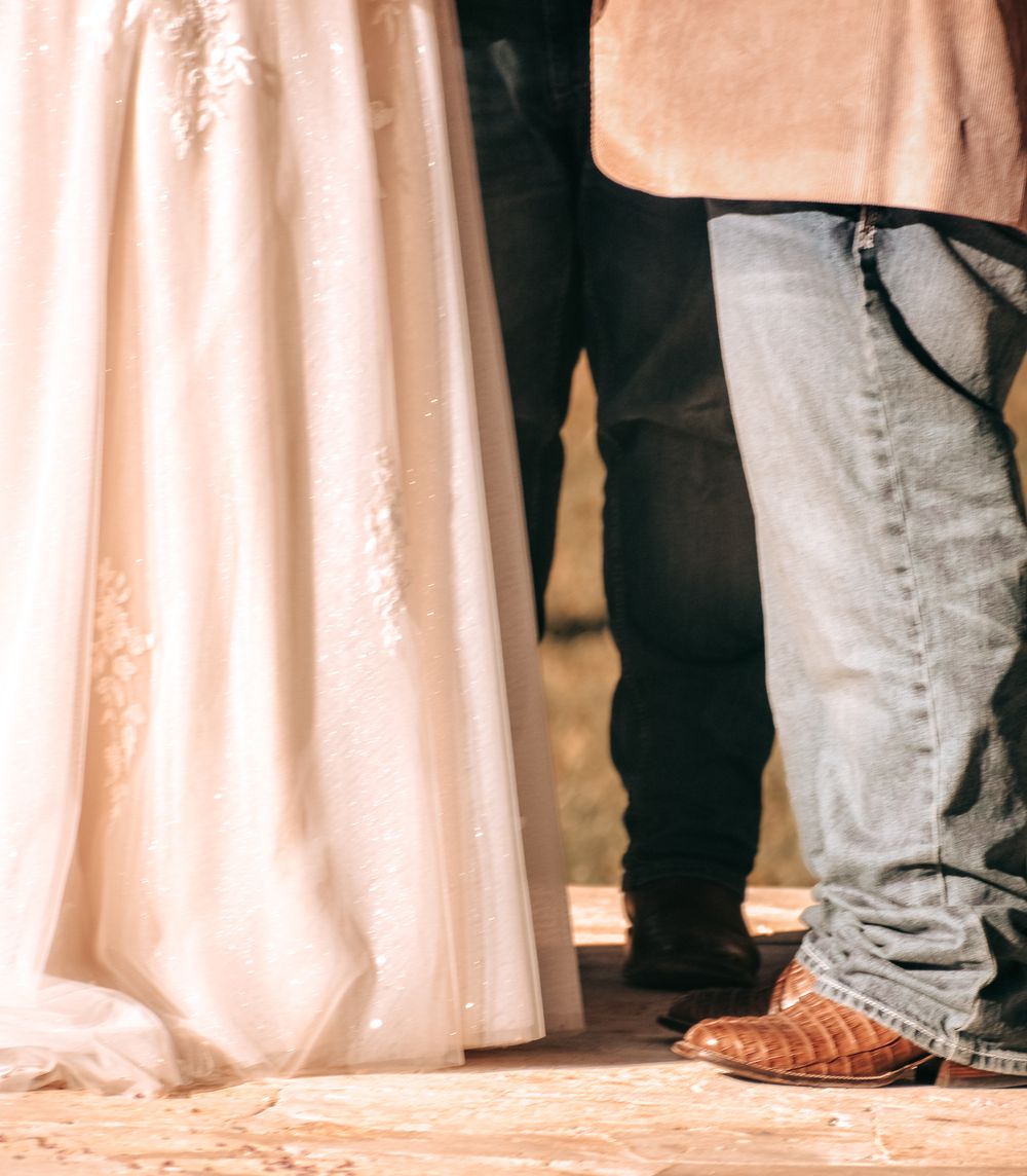 Close-up view of wedding attire showing white gown and casual jeans during outdoor ceremony.
