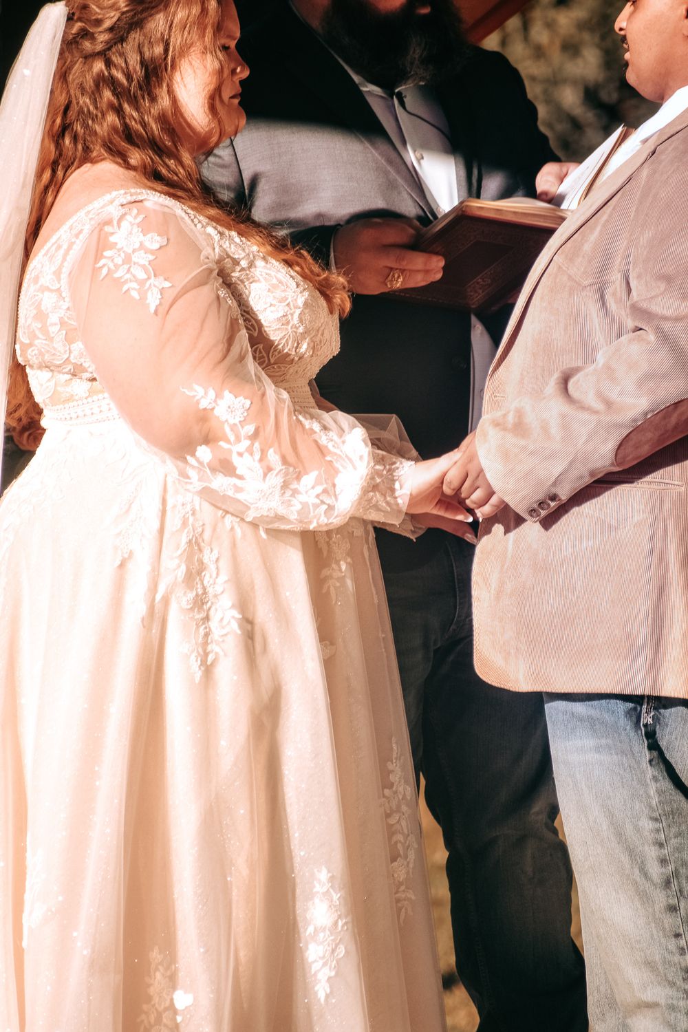 Intimate moment during wedding ceremony showing exchange of rings with detailed lace dress visible.