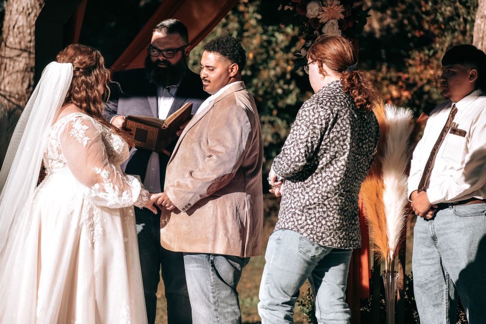 Outdoor wedding ceremony with wooden arch and casual attire in natural setting.