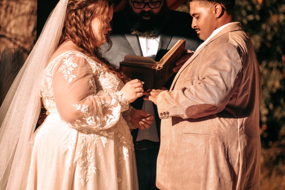 Wedding couple exchanging rings during intimate outdoor ceremony with officiant present.