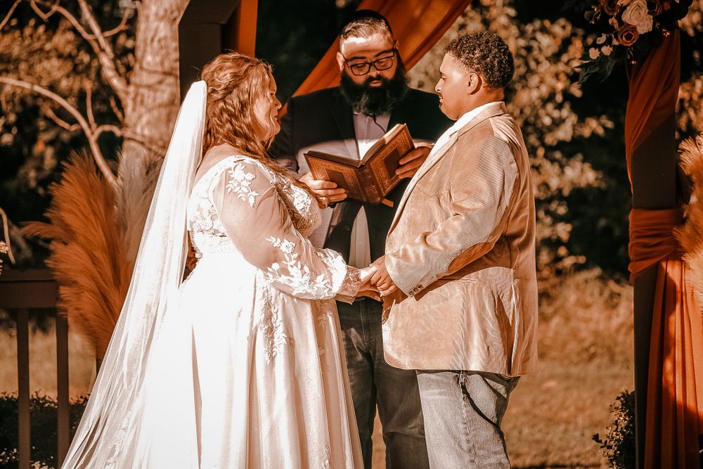 A romantic wedding ceremony moment captured under a wooden arbor during an outdoor celebration.