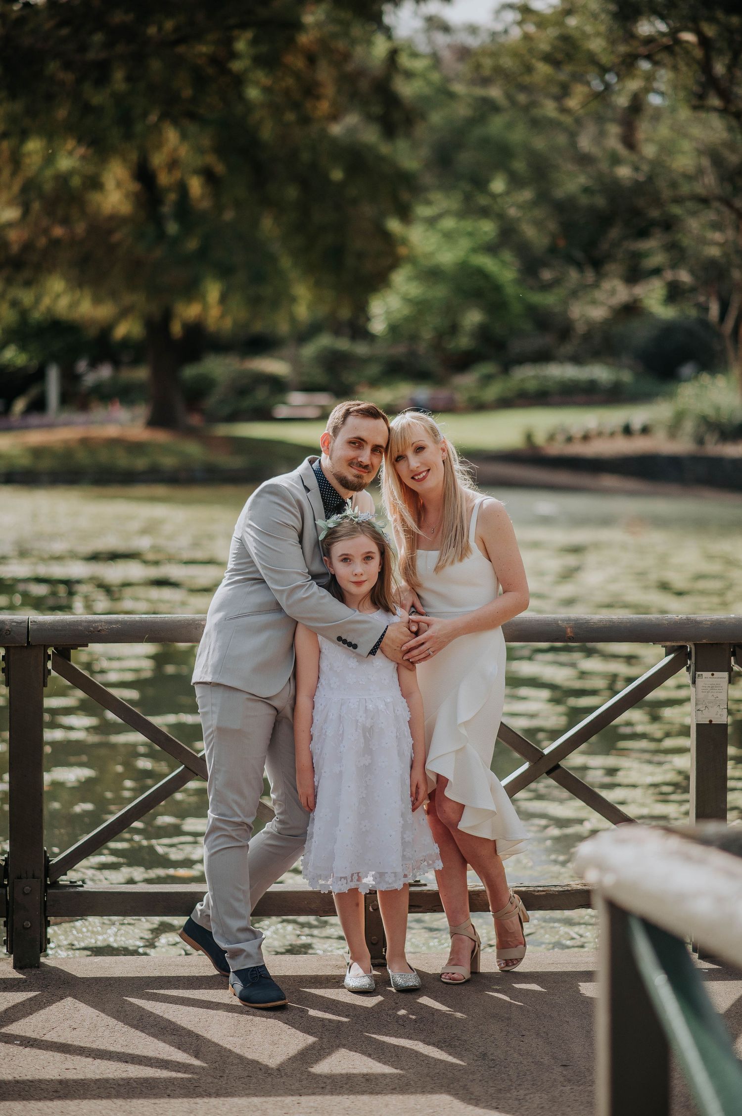 A family poses together on a wooden bridge over a pond in a scenic park.