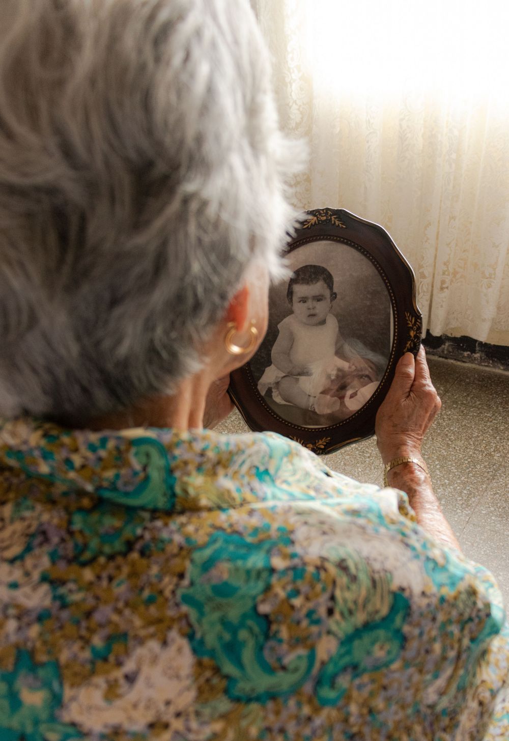 Person with gray hair looking at an old photograph in sunlit room.