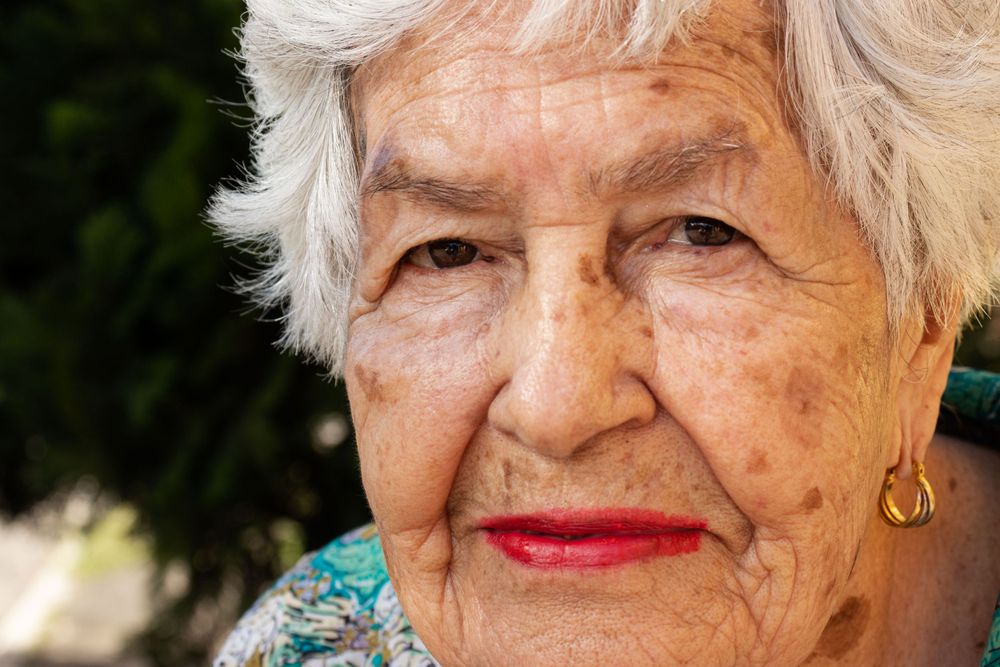 Senior with white hair wearing floral clothing outdoors.