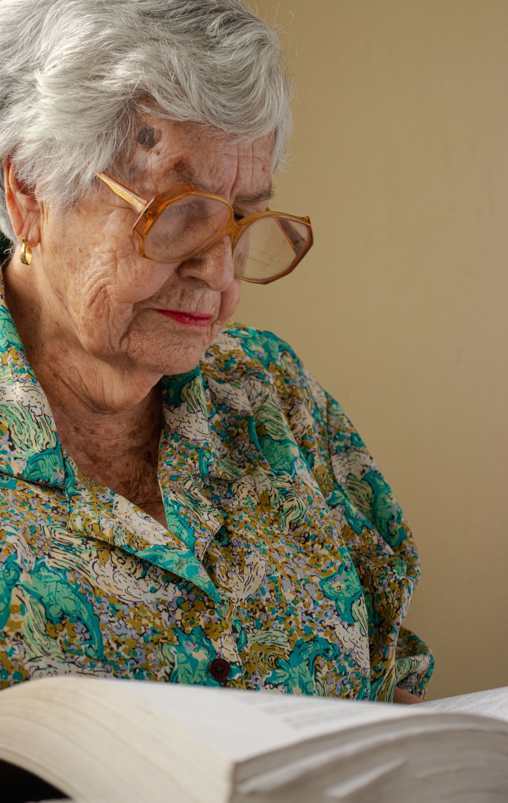 Senior wearing a floral green blouse reads intently from a book.
