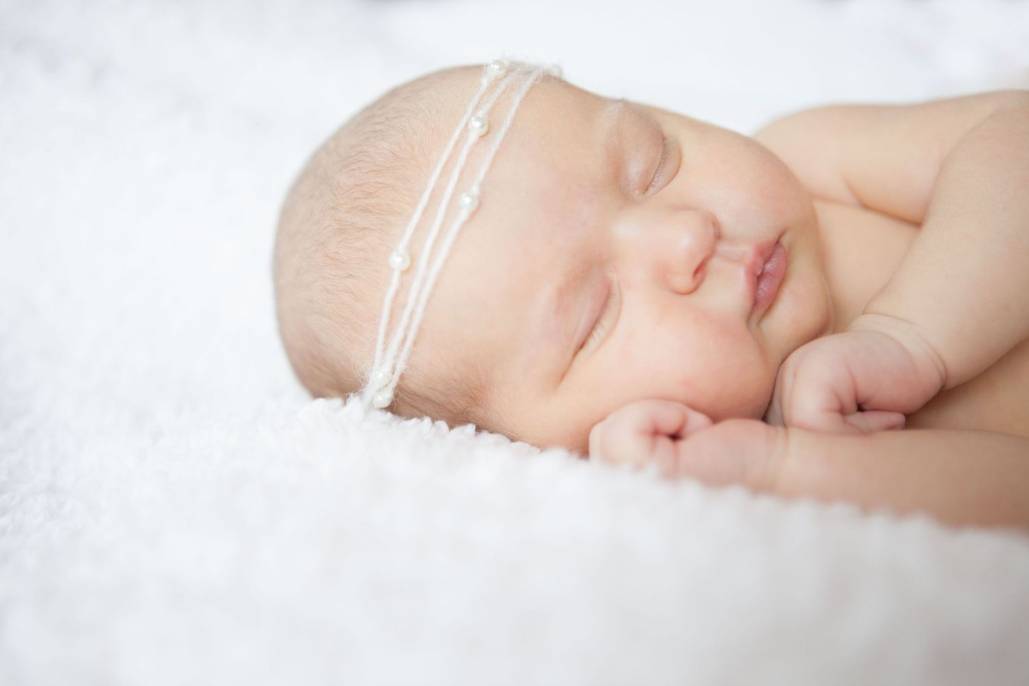 Peaceful sleeping newborn wrapped in soft white fabric with delicate headband.