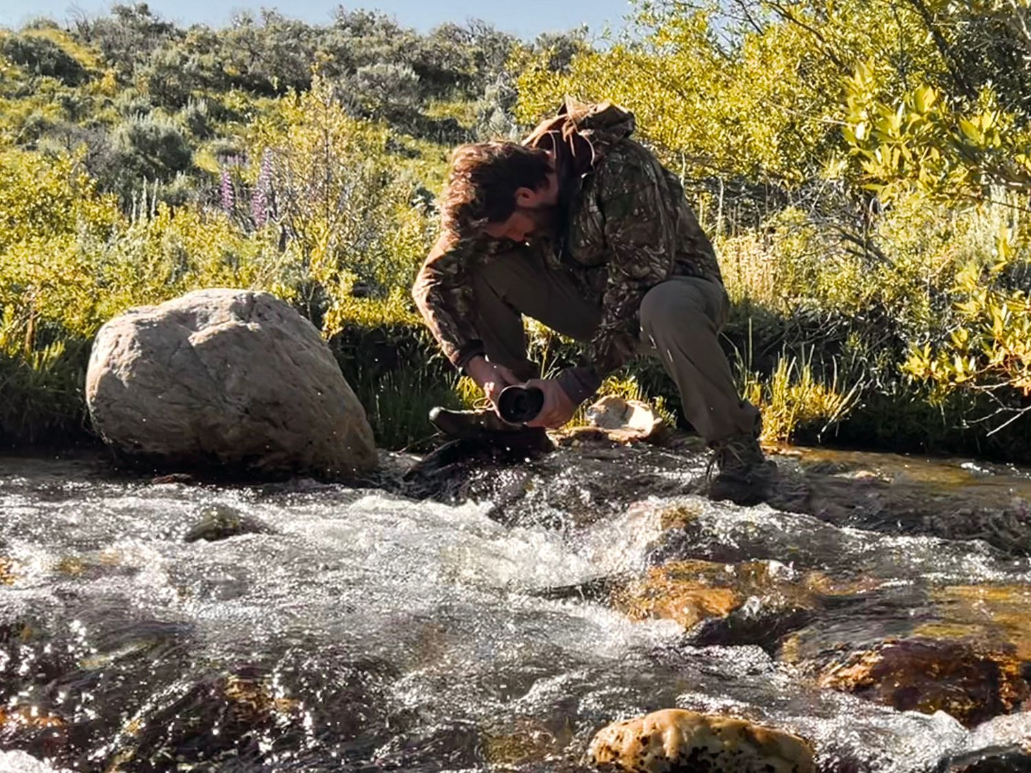 Arkansas nature photographer, Alex Kent crouches balanced on rocks over a river holding the camera low to the water.