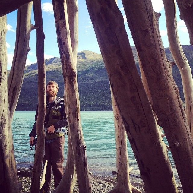 Arkansas nature photographer, Alex Kent  poses facing the camera with large vertical logs in foreground and lake behind