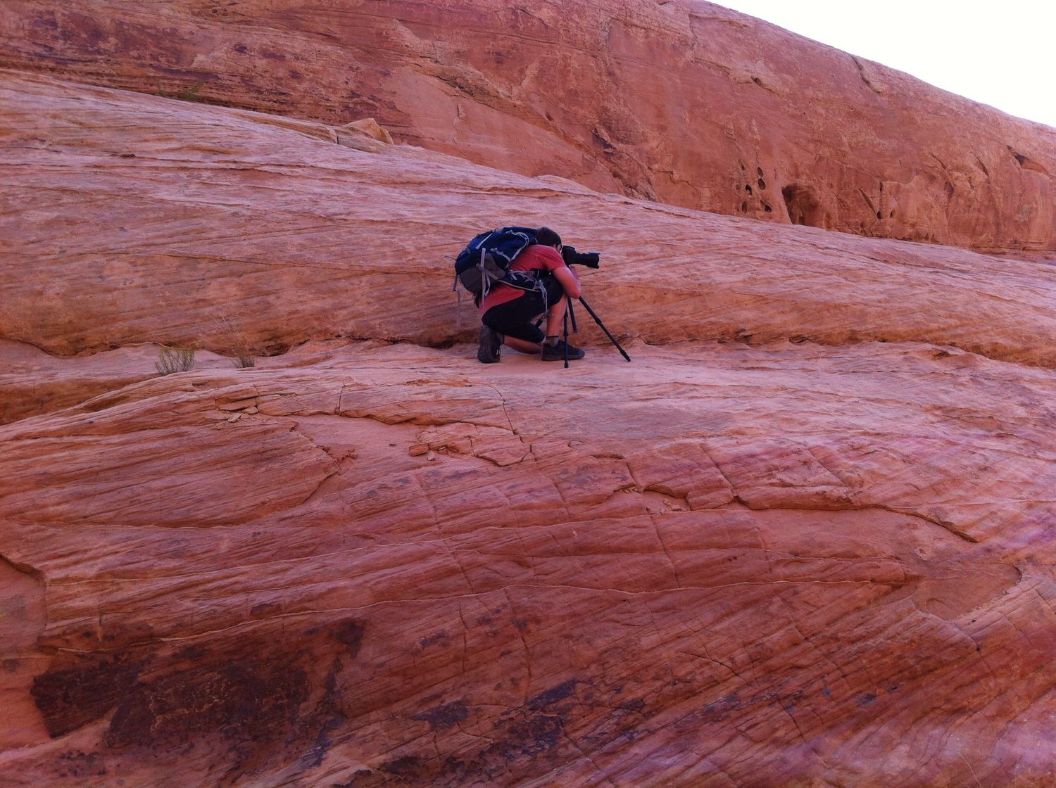 Arkansas nature photographer, Alex Kent crouches behind camera on a tripod up on a rounded bluff edge of red rock
