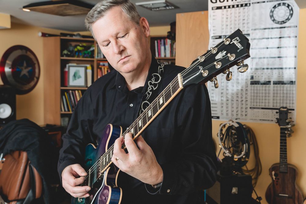 Musician playing electric guitar in home studio setting.