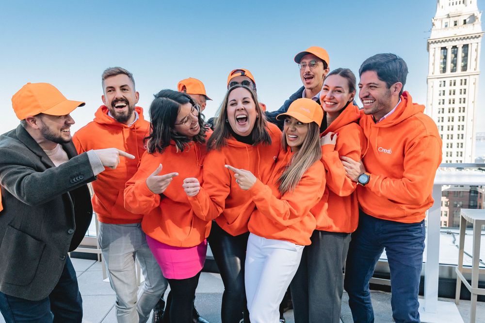 Happy group in matching orange sweatshirts posing together near city buildings.
