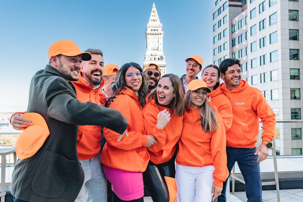 Energetic group photo of people in orange hoodies with city skyline in background.